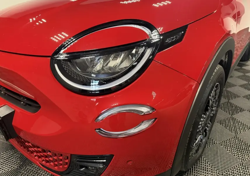 Gros plan sur l'avant droit rouge foncé du FIAT 600 Hybrid 2025, mettant en valeur le phare LED et la calandre distinctive.