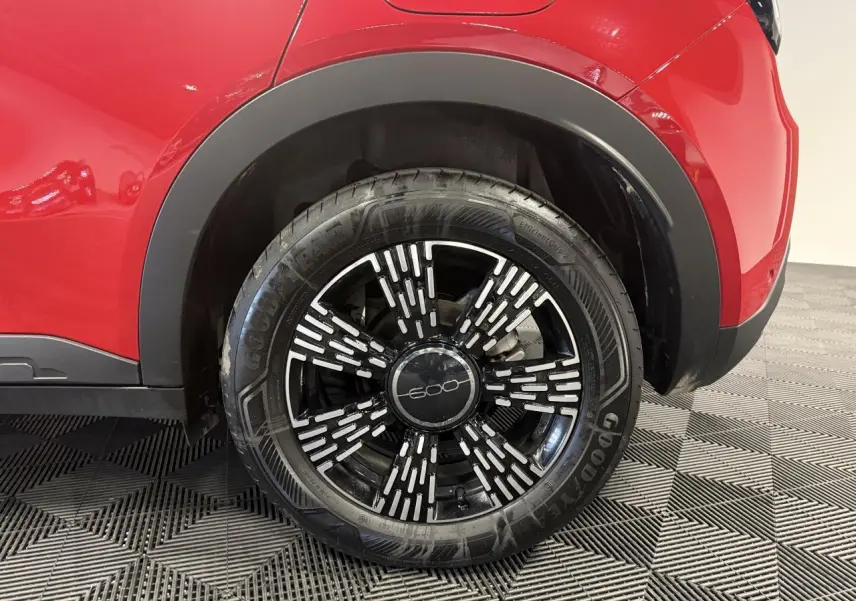 Gros plan sur la roue arrière droite d'une FIAT 600 rouge foncé avec jante noire et détails blancs stylisés.