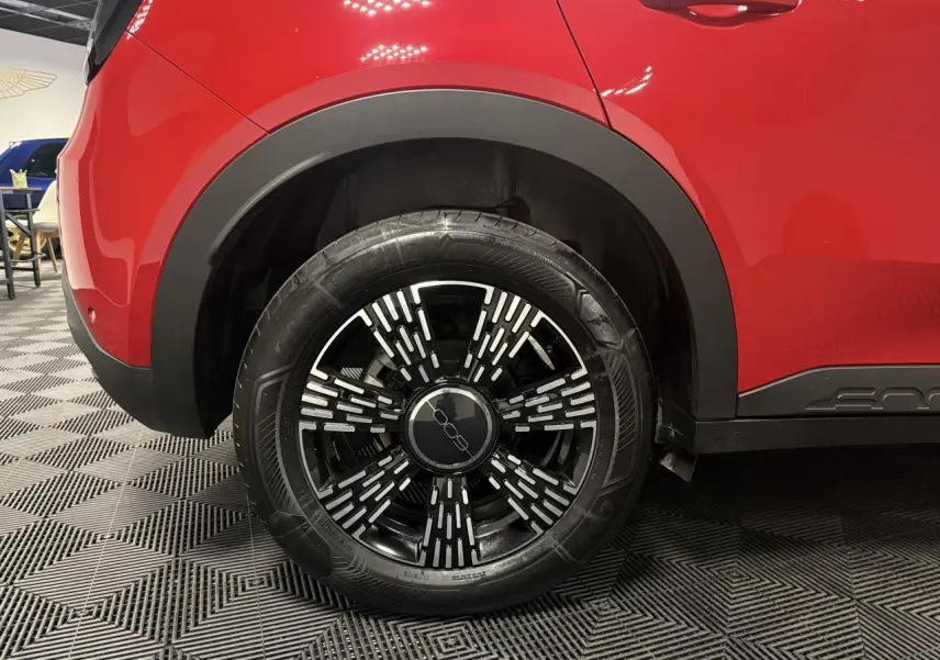 Gros plan sur la roue arrière droite d'une FIAT 600 rouge foncé avec jante noire et détails argentés.