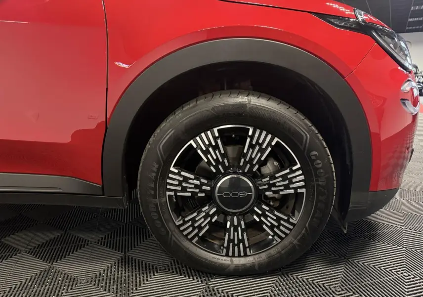 Gros plan sur la roue avant droite d'une FIAT 600 rouge foncé avec jante noire et motifs argentés.