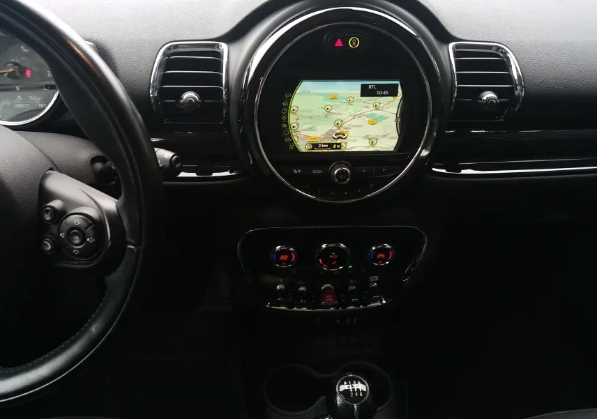 Vue intérieure centrée sur le tableau de bord noir du MINI CLUBMAN F54 avec écran GPS rond et levier de vitesse manuel.