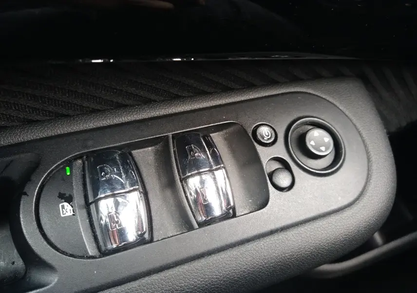 Gros plan sur les commandes de lève-vitres et réglage des rétroviseurs côté conducteur d'une MINI Clubman F54 argentée.