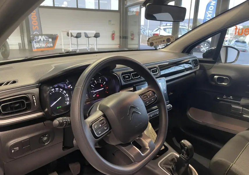 Vue intérieure côté conducteur du tableau de bord et volant noir d'une Citroën C3 beige clair 2024 avec boîte manuelle.