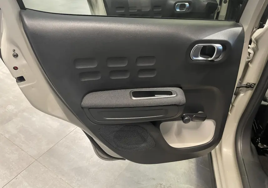 Vue rapprochée de la porte arrière gauche beige clair d'une Citroën C3 2024 avec poignée chromée et manivelle de vitre.