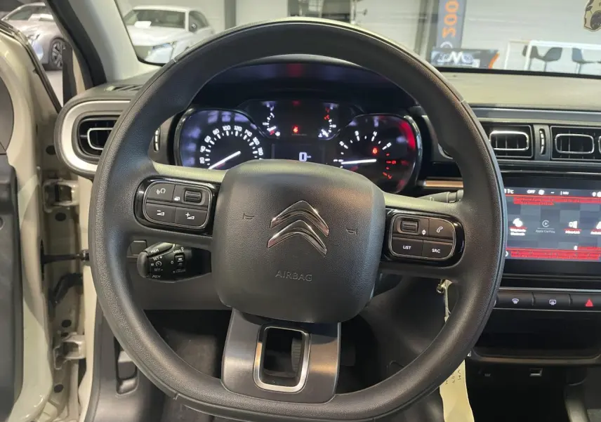Vue intérieure centrée sur le volant noir de la Citroën C3 beige clair 2024 avec tableau de bord et écran tactile.