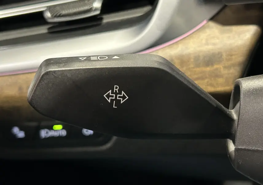 Gros plan sur la manette de clignotant noire à gauche du volant, avec tableau de bord en bois clair en arrière-plan.