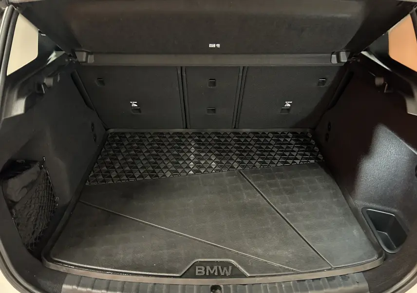 Vue du coffre ouvert de la BMW Série 2 Active Tourer blanc, montrant un tapis de coffre noir avec logo BMW.
