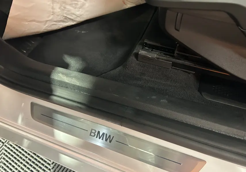 Gros plan sur le seuil de porte côté conducteur d'une BMW Série 2 Active Tourer blanche avec logo BMW en métal brossé.