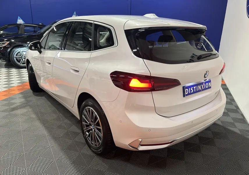 Vue 3/4 arrière droite d'une BMW Série 2 Active Tourer blanche avec feux arrière allumés en intérieur showroom.