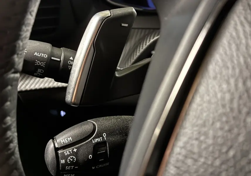 Gros plan sur la commande de régulateur de vitesse et la palette de changement de vitesse dans l'habitacle noir du Peugeot 2008 bleu.
