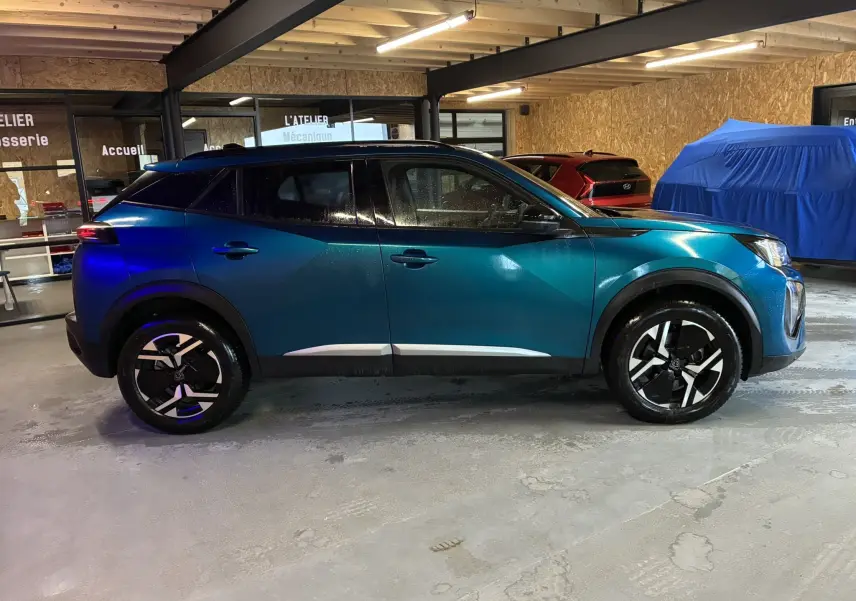 Peugeot 2008 1.2 Hybrid 136 Allure bleu vue de profil côté gauche dans un garage avec jantes noires et détails chromés.