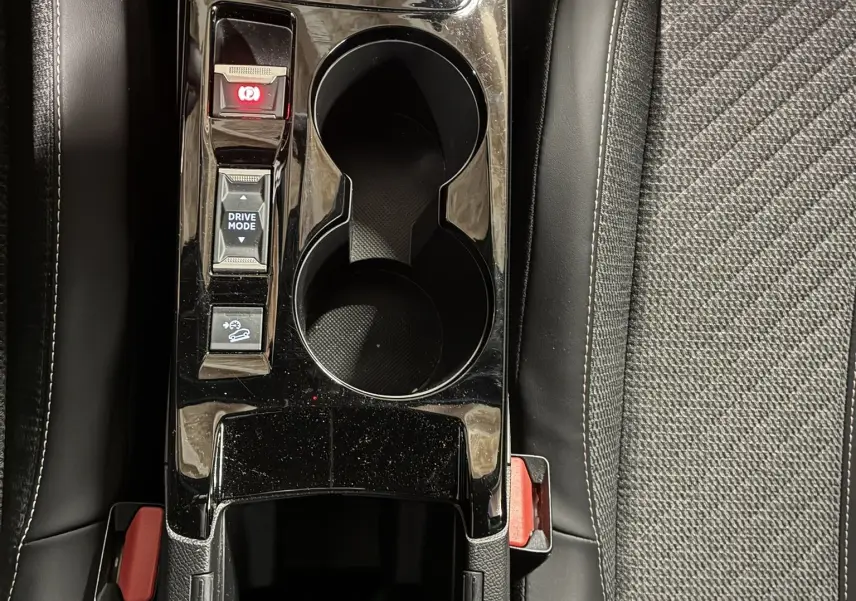 Vue plongeante sur la console centrale noire brillante du Peugeot 2008 1.2 Hybrid 136, avec porte-gobelets et commandes.