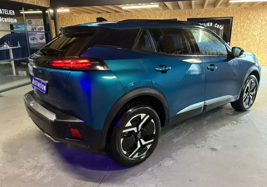 Vue 3/4 arrière droite d’un Peugeot 2008 bleu hybride 2025 avec feux arrière allumés et jantes noires stylisées.