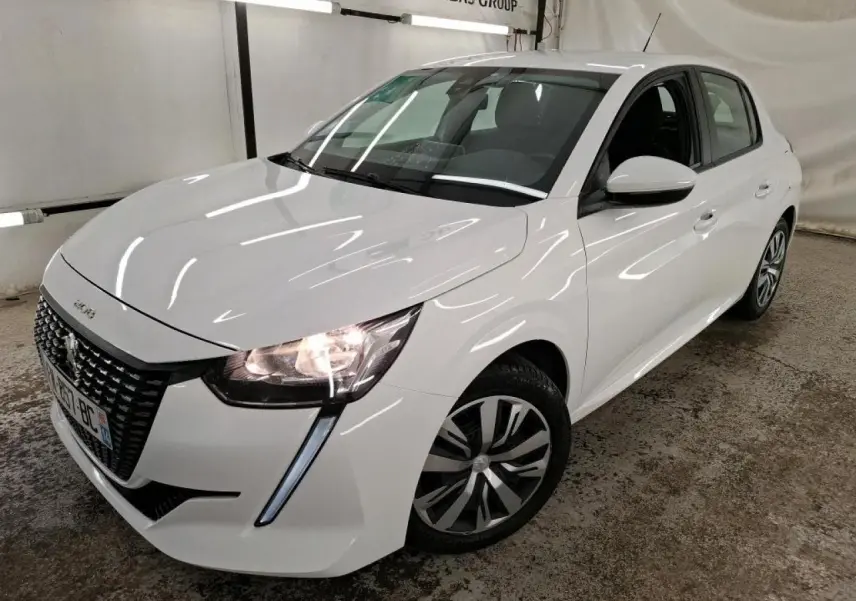Peugeot 208 blanche vue en 3/4 avant droit, avec calandre noire et feux allumés dans un garage.