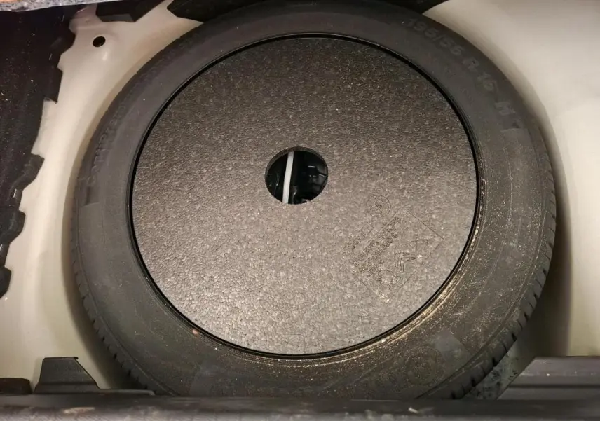 Vue rapprochée du pneu de secours noir logé dans le coffre d'une Peugeot 208 blanche de 2020.