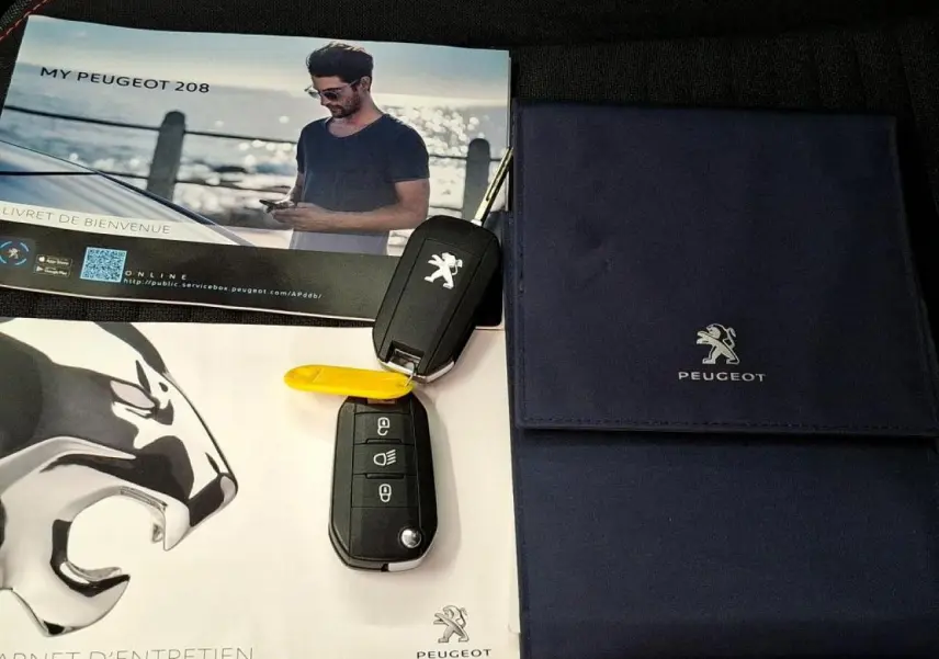 Vue rapprochée sur deux clés Peugeot noires posées sur des documents officiels bleu et blanc avec logo lion argenté.