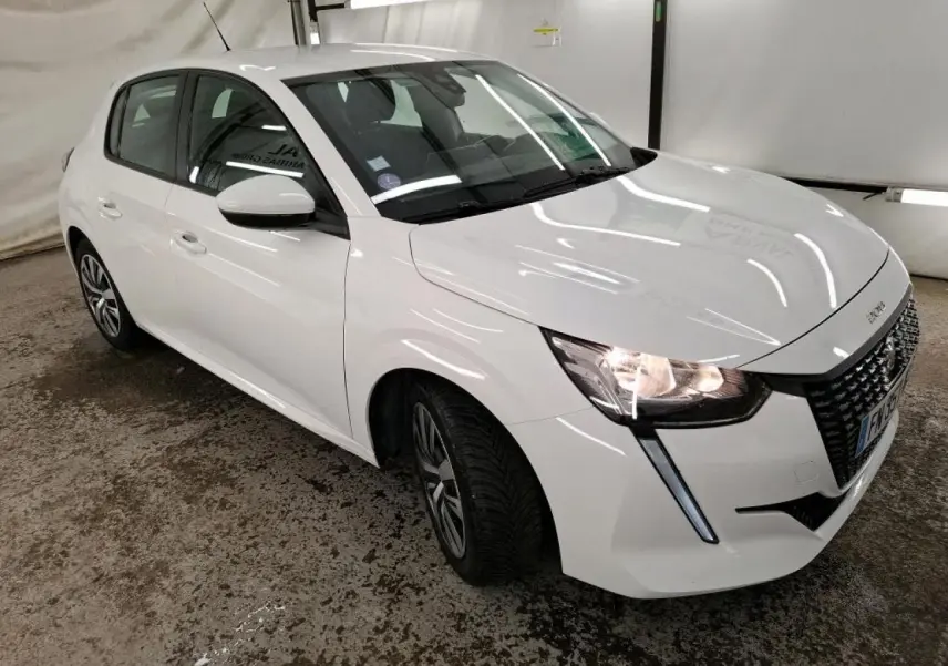 Peugeot 208 blanche vue en 3/4 avant droit, avec calandre noire et feux allumés dans un garage.