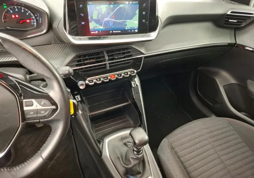 Vue intérieure côté conducteur de la Peugeot 208 blanche, avec tableau de bord carbone et écran tactile central.