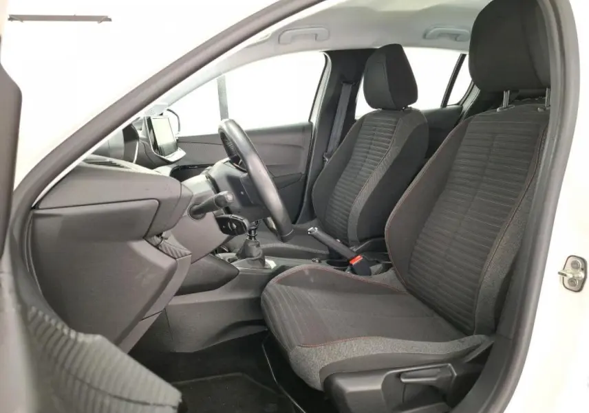 Vue intérieure côté conducteur de la Peugeot 208 blanche, montrant les sièges tissu gris et le volant compact noir.
