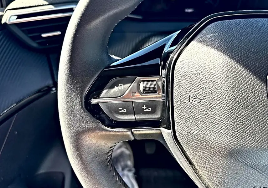 Gros plan sur les commandes au volant à gauche de la Peugeot 208 1.2 100 Allure, intérieur noir texturé.