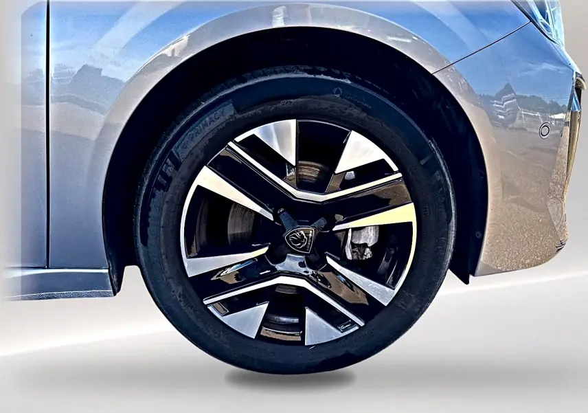 Gros plan sur la roue avant gauche de la Peugeot 208 gris artense, mettant en valeur la jante alu au design moderne.