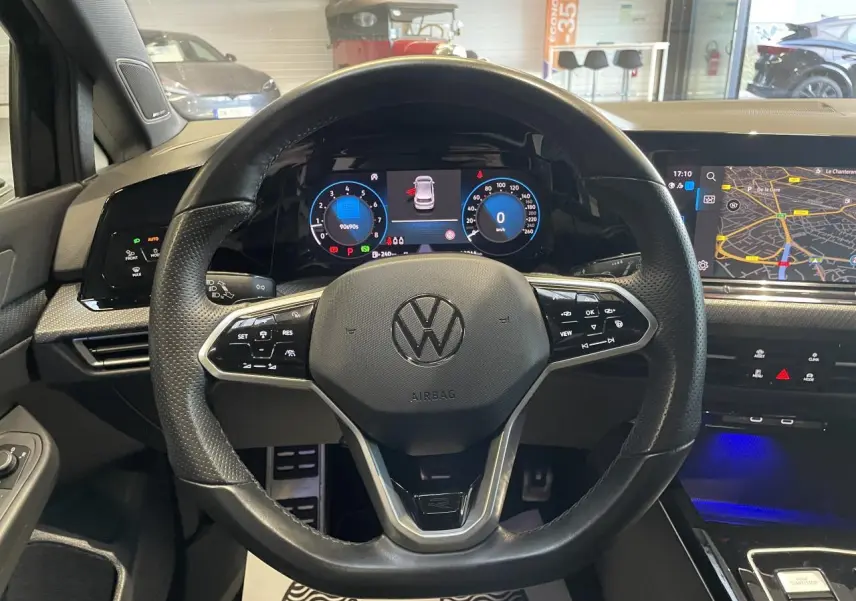 Vue intérieure centrée sur le volant cuir noir multifonctions de la Volkswagen Golf 2024 avec tableau de bord digital et écran navigation.