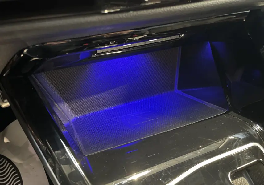 Gros plan sur le compartiment de recharge sans fil avec éclairage d'ambiance bleu dans une Volkswagen Golf VIII R-Line noire.