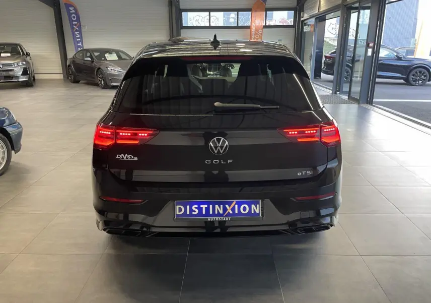 Vue arrière d'une Volkswagen Golf 1.5 eTSI noire métallisée avec feux LED allumés en showroom.