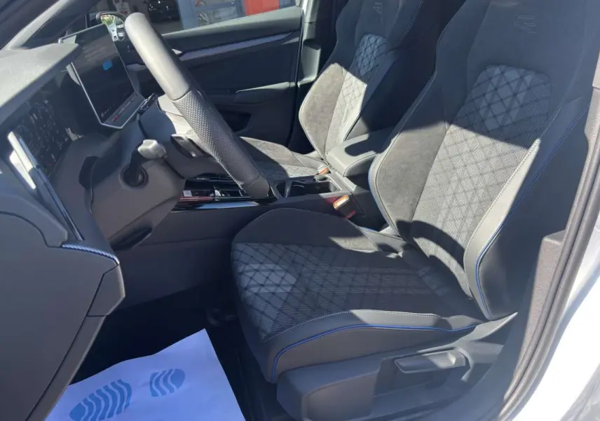 Vue intérieure côté conducteur de la Volkswagen Golf E-TSI 150 DSG R-Line avec sièges noirs à surpiqûres bleues.