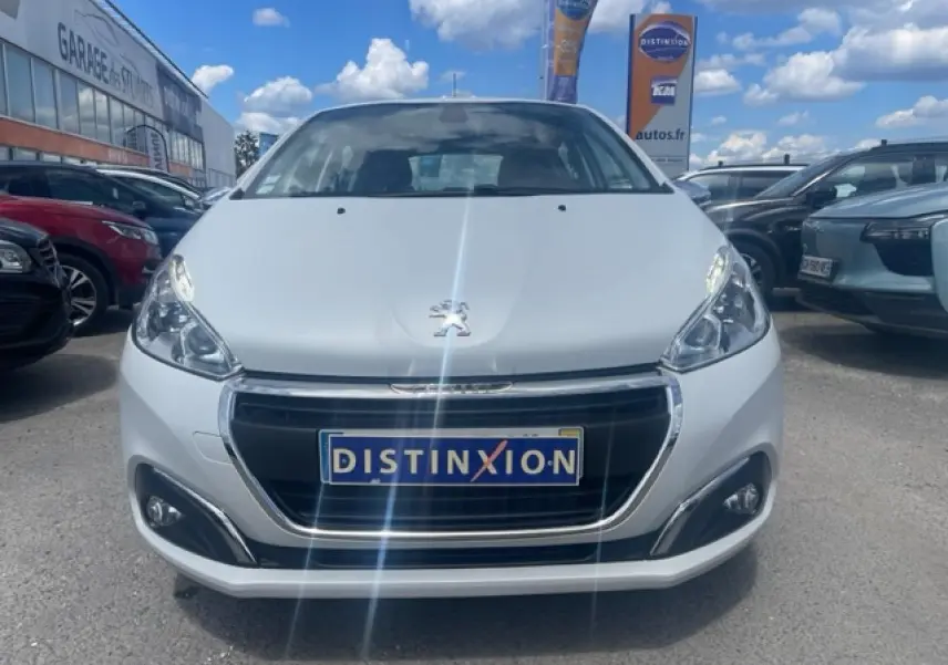 Vue frontale d'une Peugeot 208 blanche perle avec calandre chromée et logo lion bien visible au centre.