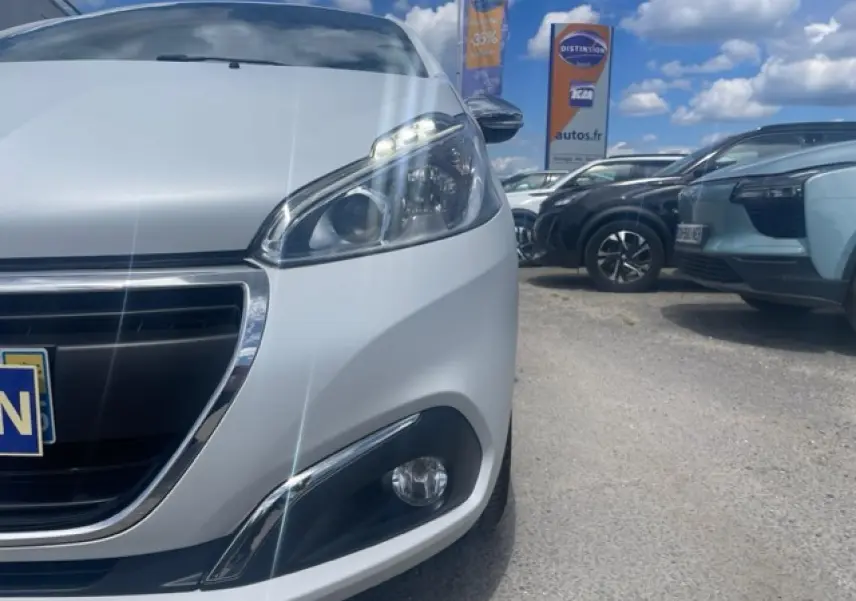 Gros plan sur l'avant droit d'une Peugeot 208 blanc perle avec phares et calandre chromée sous un ciel bleu.