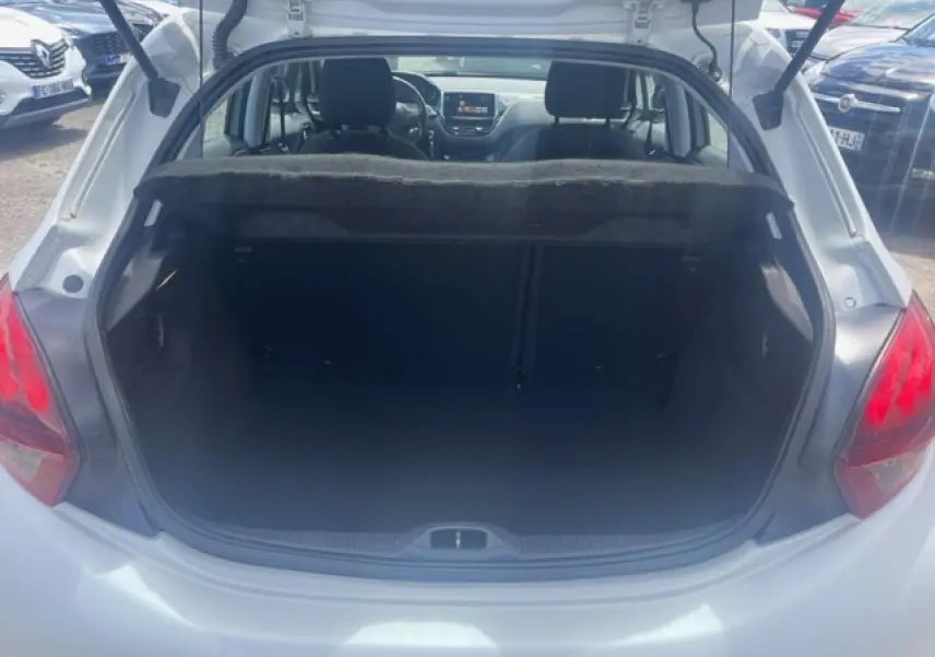 Coffre ouvert vu de l'arrière d'une Peugeot 208 blanc perle, avec intérieur sombre et banquette arrière visible.