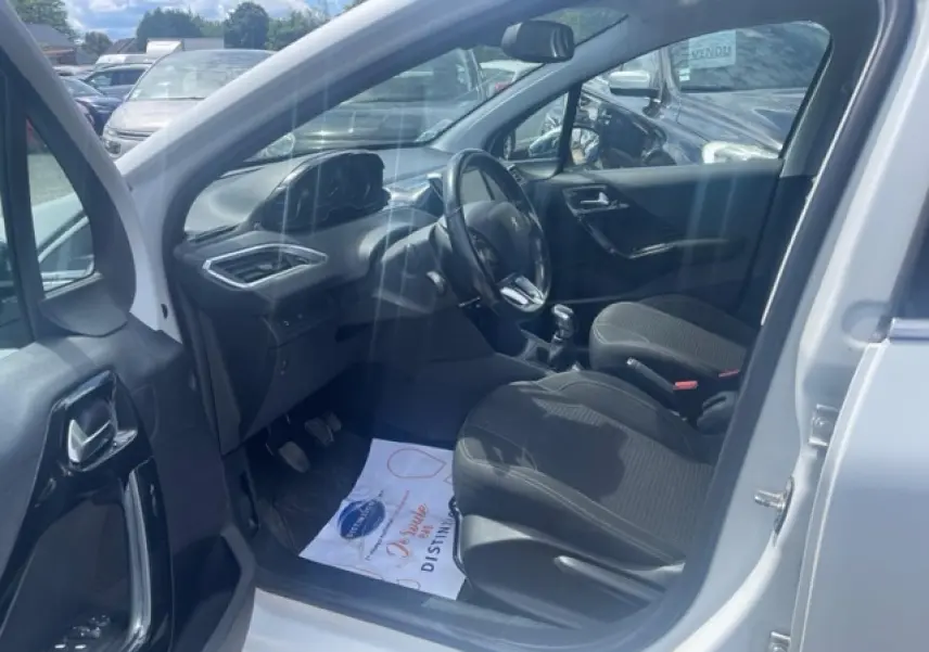 Vue intérieure côté conducteur d'une Peugeot 208 blanc perle, montrant les sièges noirs et le volant multifonction.