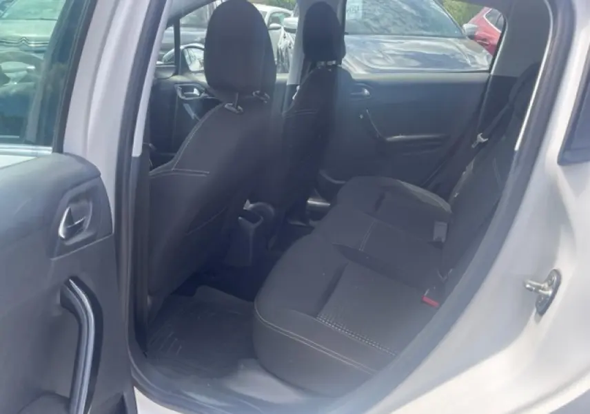 Vue intérieure côté arrière droit de la Peugeot 208 blanche perle, montrant les sièges arrière noirs et les portes ouvertes.