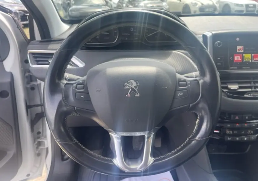 Vue intérieure centrée sur le volant cuir multifonction d'une Peugeot 208 blanc perle, avec tableau de bord et écran tactile visibles.