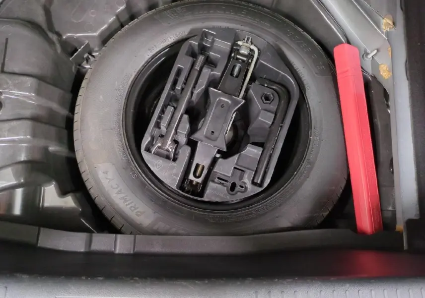 Vue plongeante sur la roue de secours noire et son kit d'outils dans le coffre de la Renault Mégane noir métal 2023.