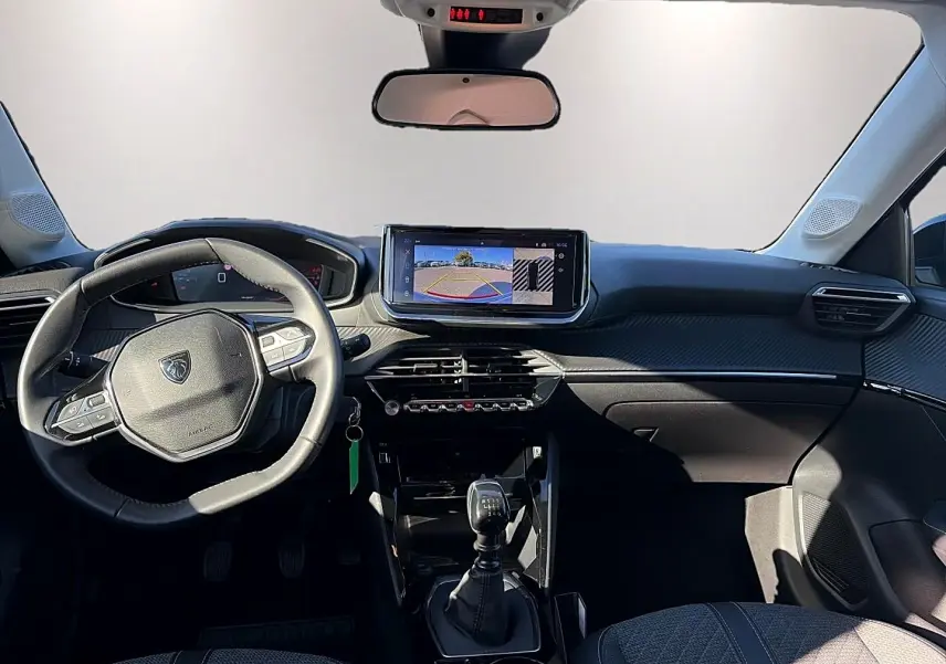 Vue intérieure avant de la Peugeot 208 1.2 100 Allure 2025, volant multifonction, écran tactile et levier de vitesse manuel.