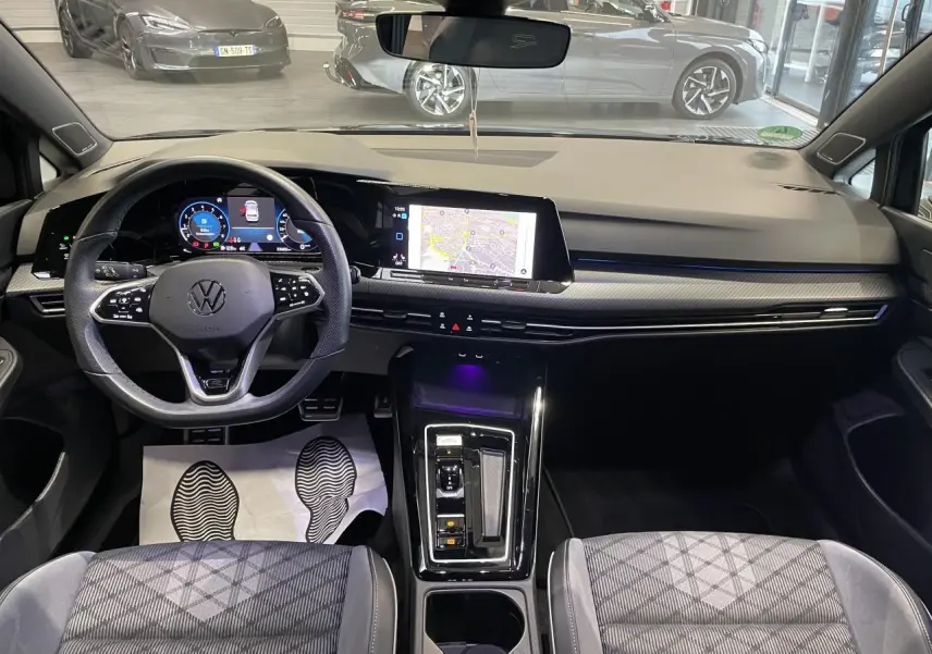 Vue intérieure avant de la Volkswagen Golf 1.5 eTSI 2024, tableau de bord noir avec écran tactile et volant multifonctions cuir.