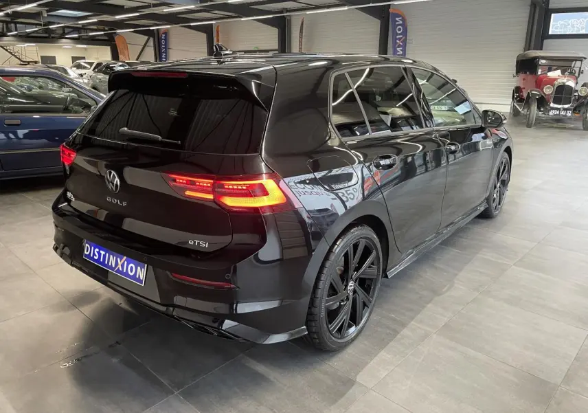 Vue 3/4 arrière droite d'une Volkswagen Golf 1.5 eTSI noire métallisée avec jantes noires 18 pouces en alliage léger.