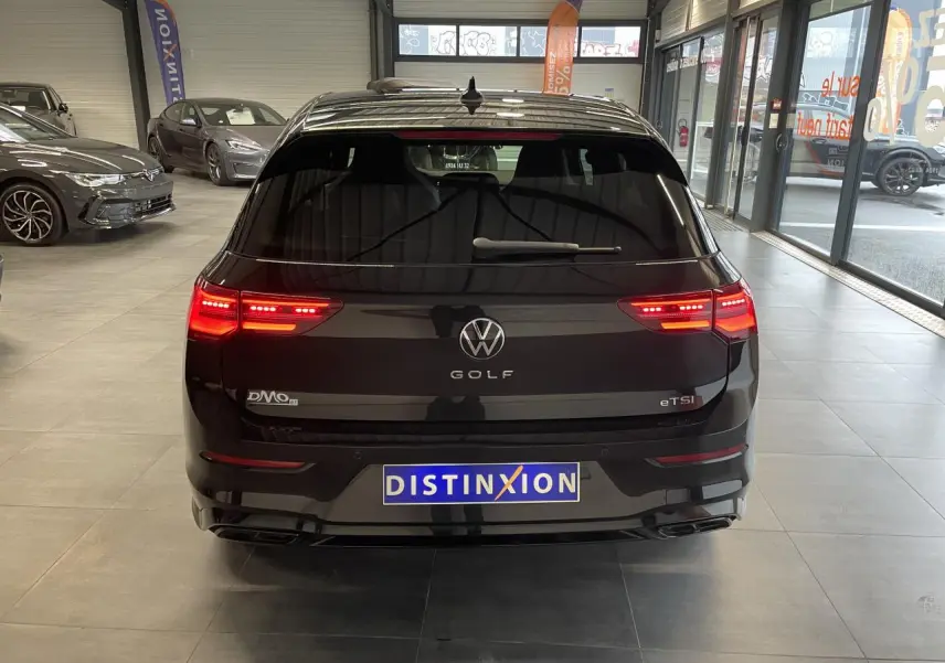 Vue arrière d'une Volkswagen Golf 1.5 eTSI noire métallisée avec feux LED allumés en intérieur showroom.