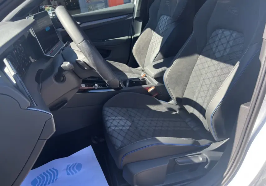 Vue intérieure côté conducteur de la Volkswagen Golf E-TSI 150 R-Line avec sièges noirs à surpiqûres bleues.