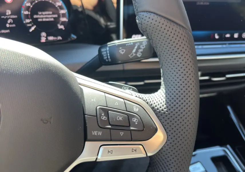 Gros plan sur le volant cuir perforé côté gauche de la Volkswagen Golf blanc oryx, avec commandes multifonctions et affichage numérique.