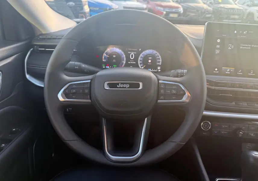 Vue intérieure centrée sur le volant Jeep du Compass 2024 avec tableau de bord numérique et écran tactile.