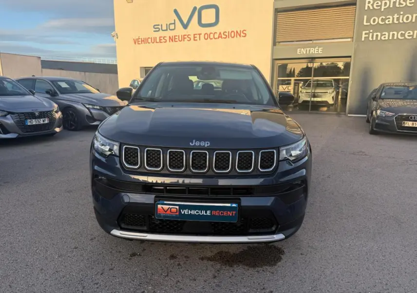 Vue de face d’un Jeep Compass bleu 2024 avec calandre distinctive et plaque « Véhicule récent » sur un parking extérieur.