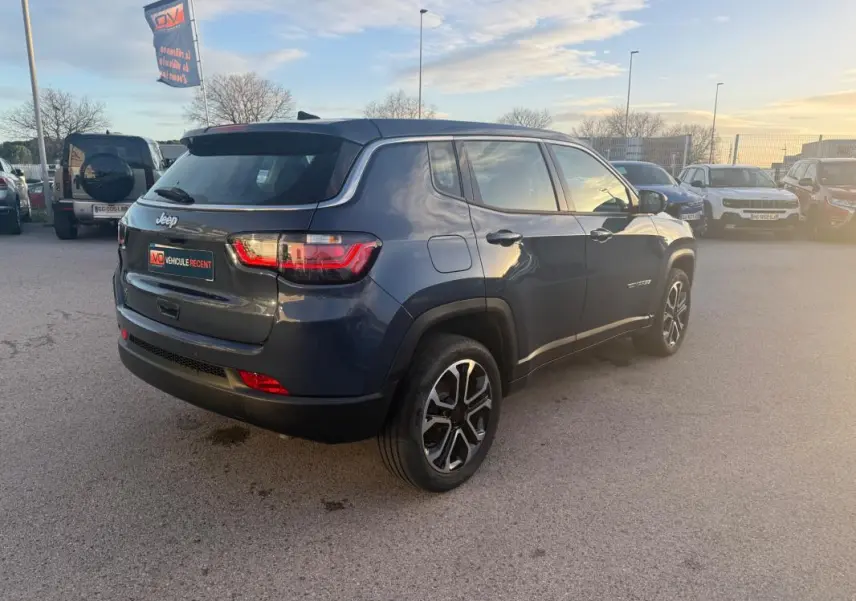 Vue 3/4 arrière droite du Jeep Compass bleu 2024 avec jantes alliage 18 pouces et feux arrière LED allumés.