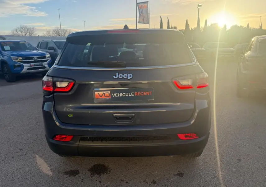 Vue arrière d'un Jeep Compass bleu foncé 2024 avec feux LED allumés, sur parking extérieur en fin de journée.