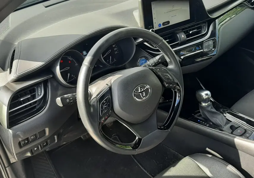 Vue intérieure côté conducteur du Toyota C-HR 1.8 Hybrid 2023, volant multifonction et écran tactile central noir.