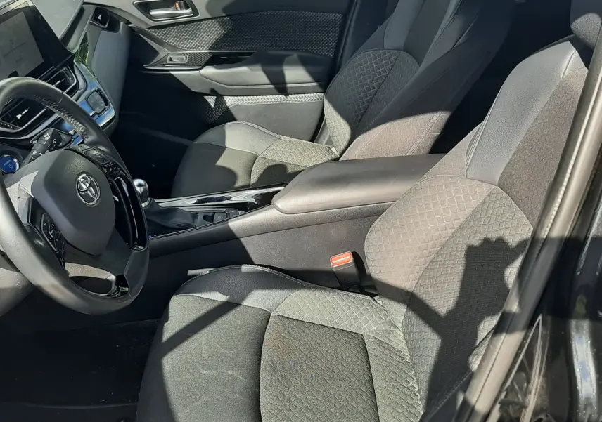 Intérieur avant droit du Toyota C-HR 1.8 Hybrid 2023 noir, sièges tissu noir avec motifs géométriques et console centrale brillante.