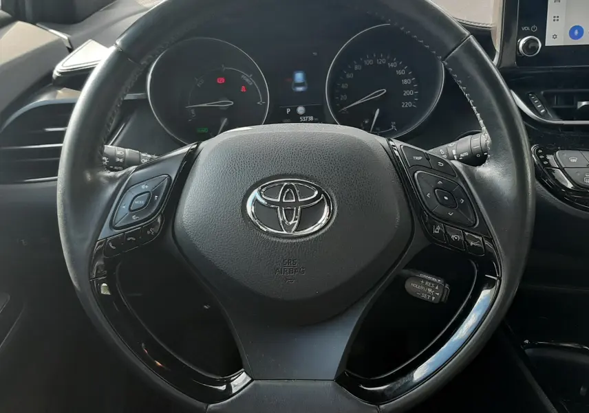 Vue intérieure centrée sur le volant noir du Toyota C-HR 1.8 Hybrid 2023 avec tableau de bord et écran tactile visibles.