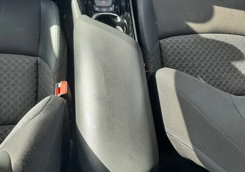 Vue intérieure centrée sur l'accoudoir et la console centrale noire du Toyota C-HR 1.8 Hybrid 2023 avec sièges tissu noirs.